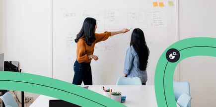 Two women viewing and pointing at data and graphs on a whiteboard. 