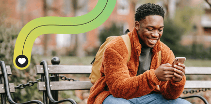 A smiling man sits on a bench while using his mobile phone.